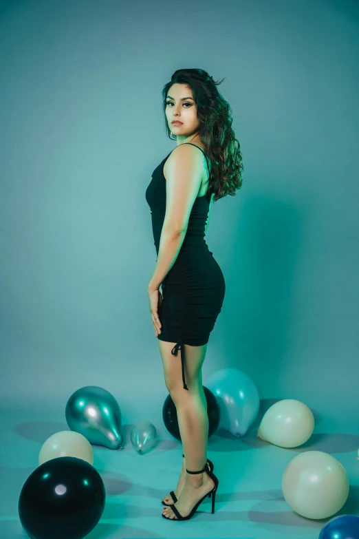 a woman wearing a black dress and posing next to balloons