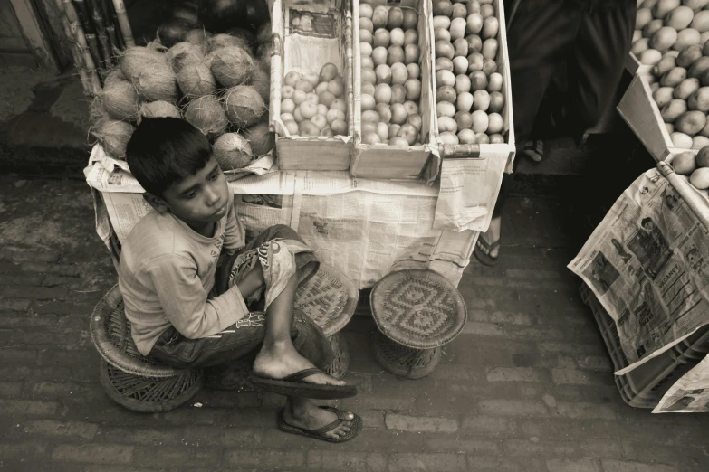 a boy sitting on the street selling fruit