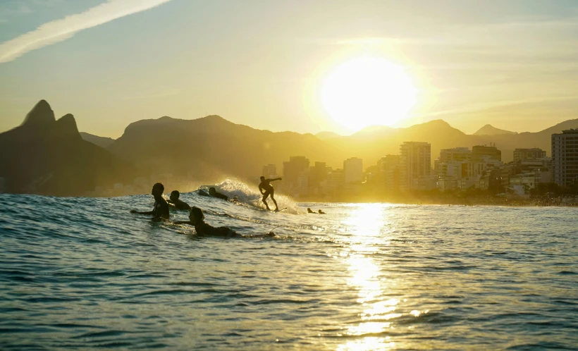 surfers in the water at sunrise near a city