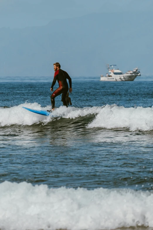 a surfer stands on a board as a small boat passes by