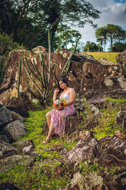 a woman sitting on the rocks with an exotic flower bouquet in her hand