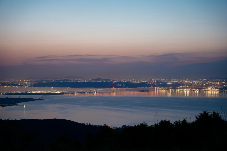 the view from a hill shows a lake with small lights