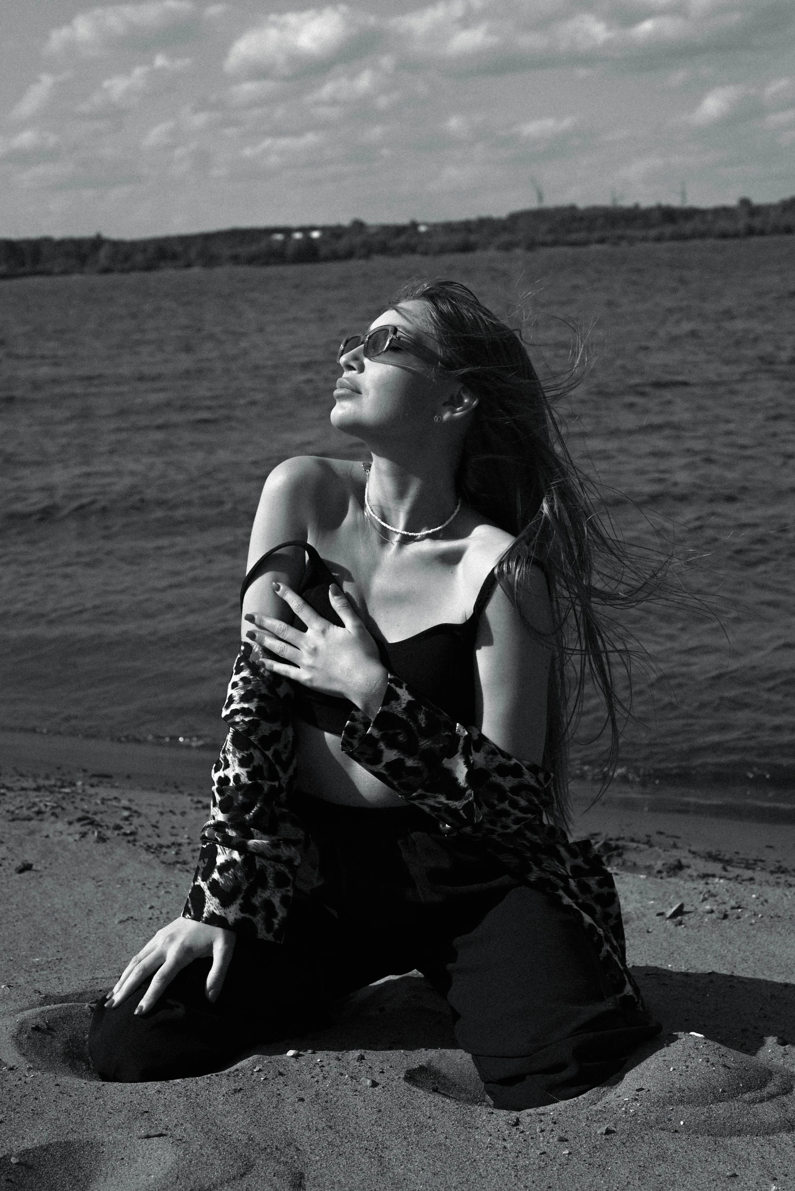 a young woman sits on the sand with her hair blowing in the wind