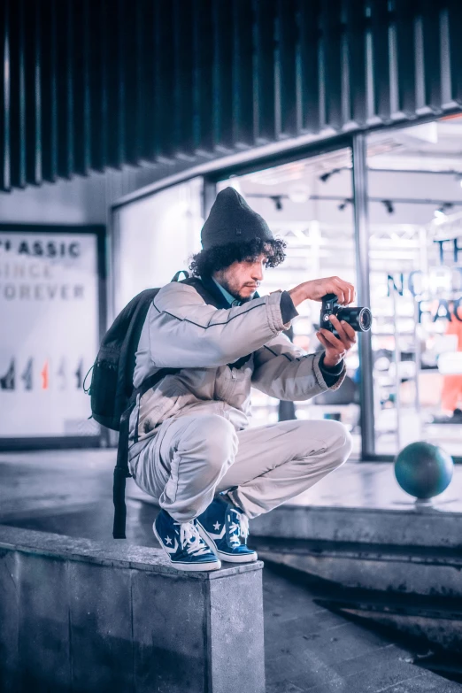 man in white sweater holding black camera sitting on wall