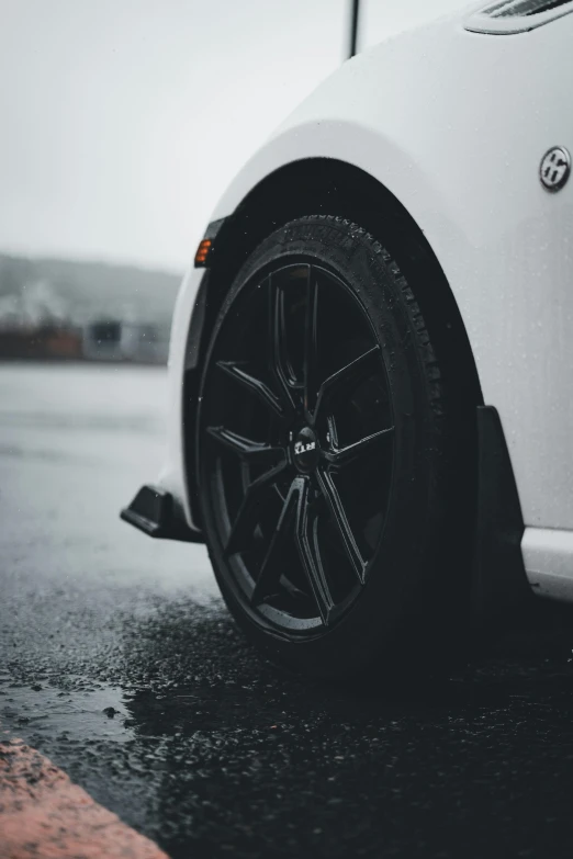 a white car with black spokes is parked in the rain