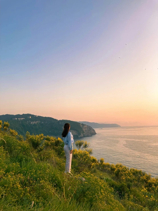 a woman is standing on the grass looking out at the ocean