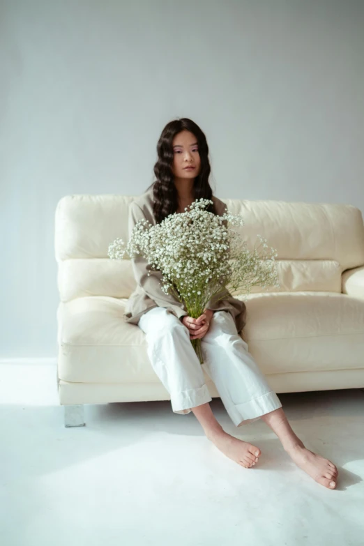 a woman sits on a white couch with flowers in front of her