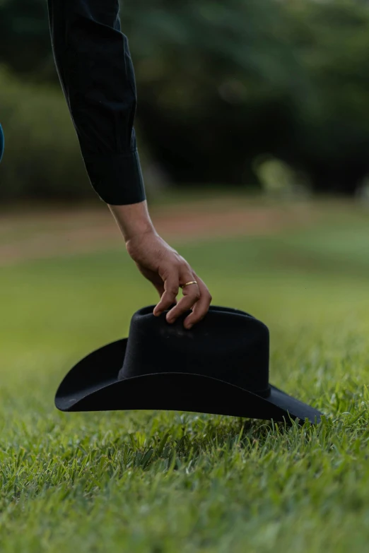 a black hat being held by a person on the grass