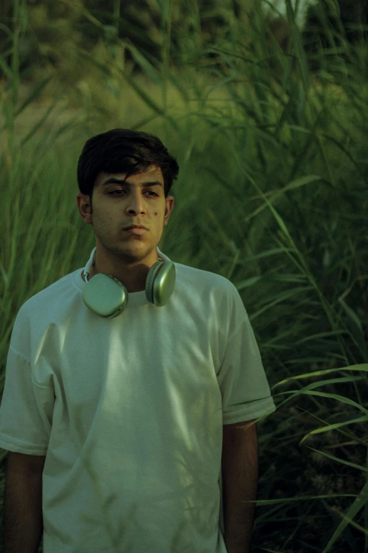 a young man wearing ear phones standing in front of tall grass