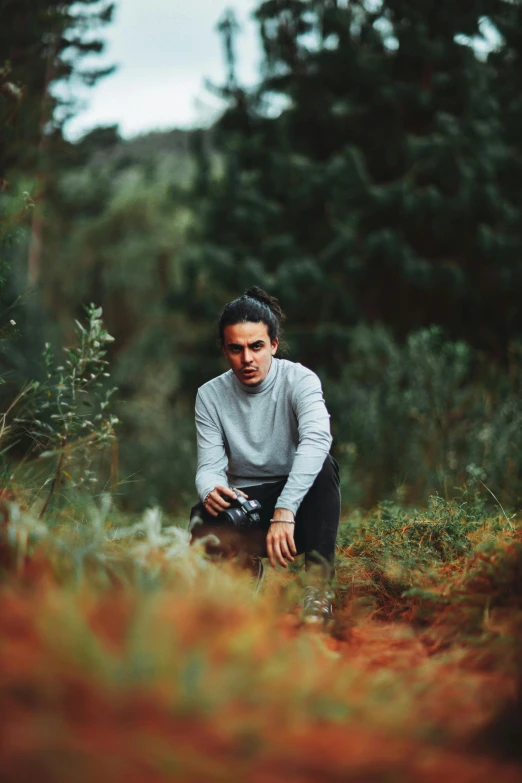 a person kneeling in the woods with a camera