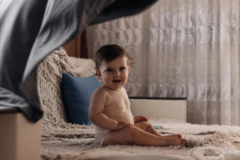 a baby sitting on top of a bed next to a blanket