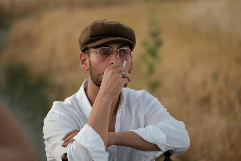a person wearing a hat and glasses and holding a cigarette