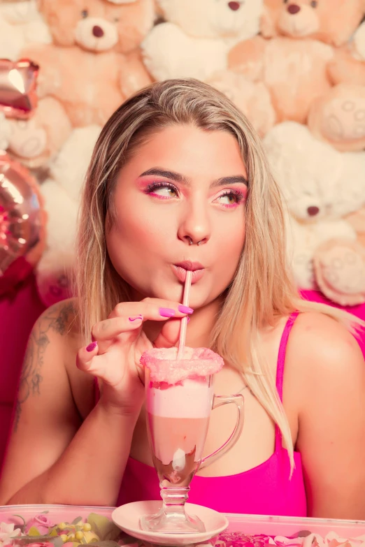 a beautiful young blonde woman sitting at a table drinking from a pink cup