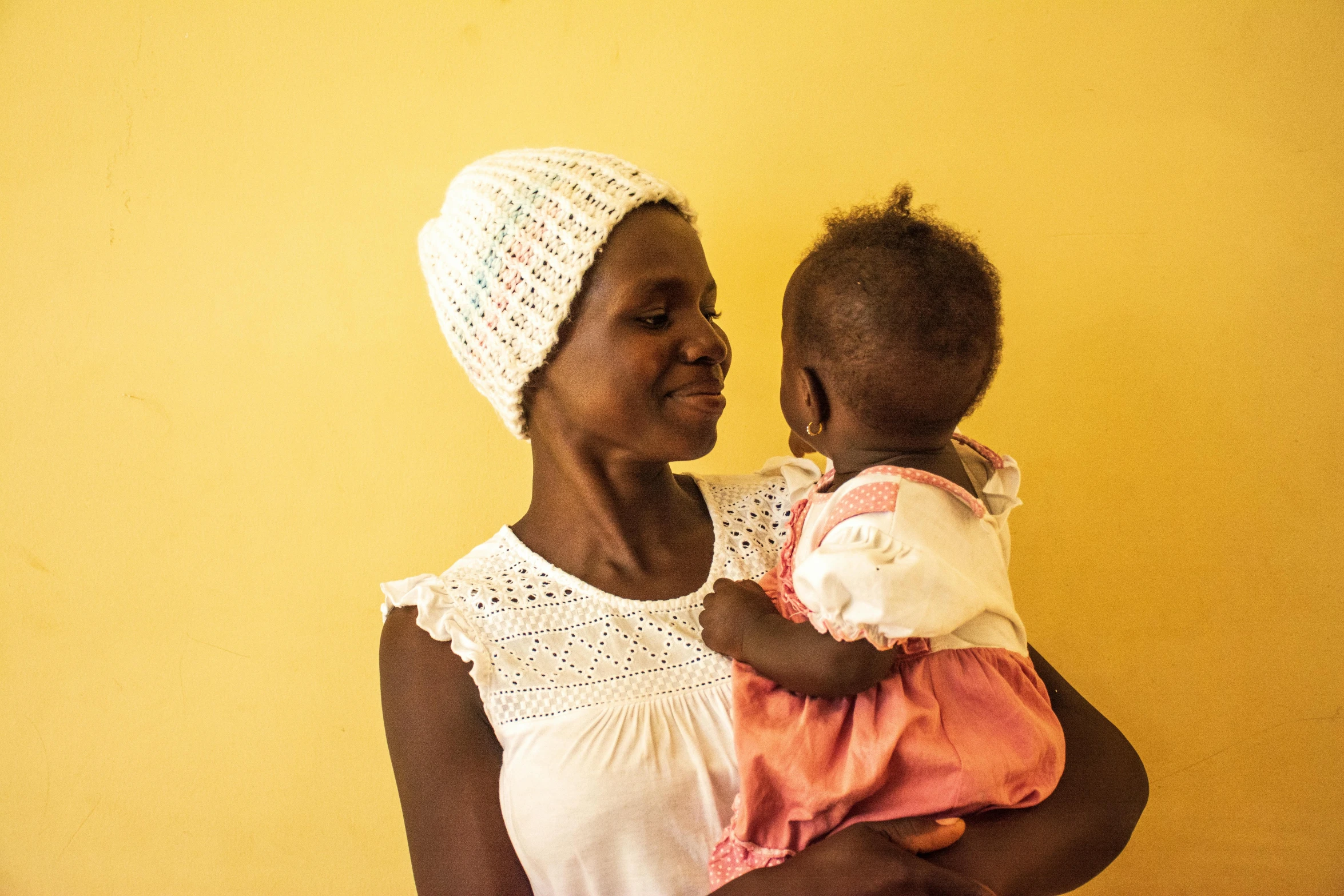 a woman holding a baby next to a yellow wall