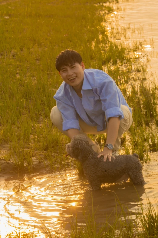 a boy bending over and petting a dog at the water's edge