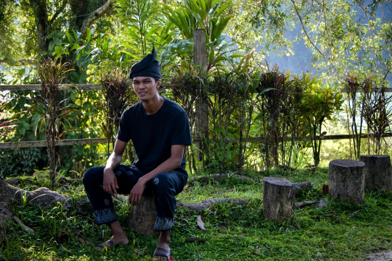 a man wearing a black hat sits on a rock