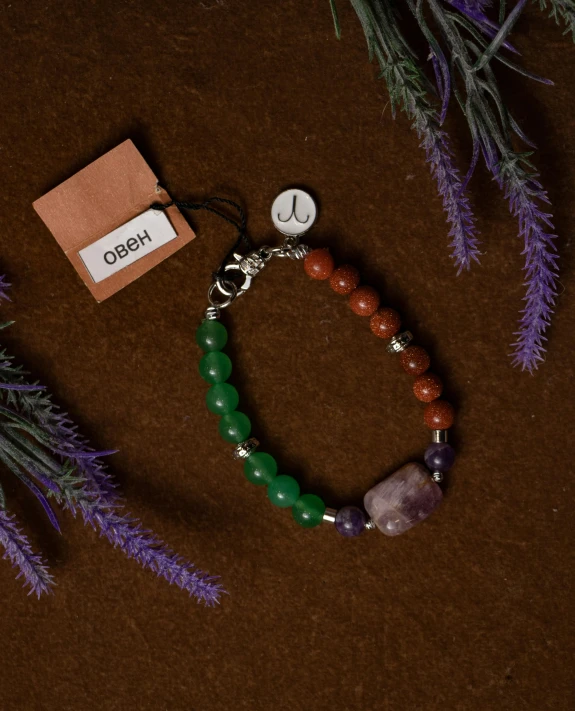 a celet with beads, a ball and a wooden tag sits next to some flowers