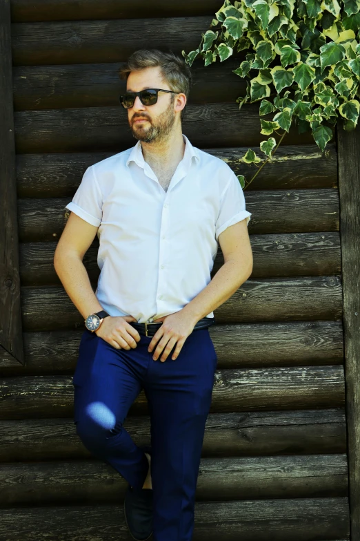 a man in white shirt and jeans standing next to wooden fence