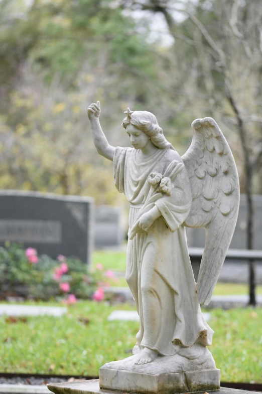 an angel statue in a cemetery by some flowers