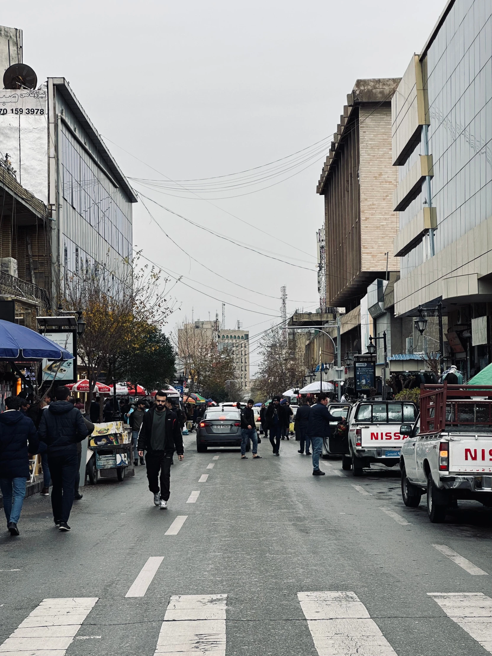 people are walking down the street where cars and buses are lined up