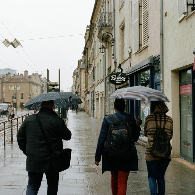 people walking in the rain with umbrellas down a city street