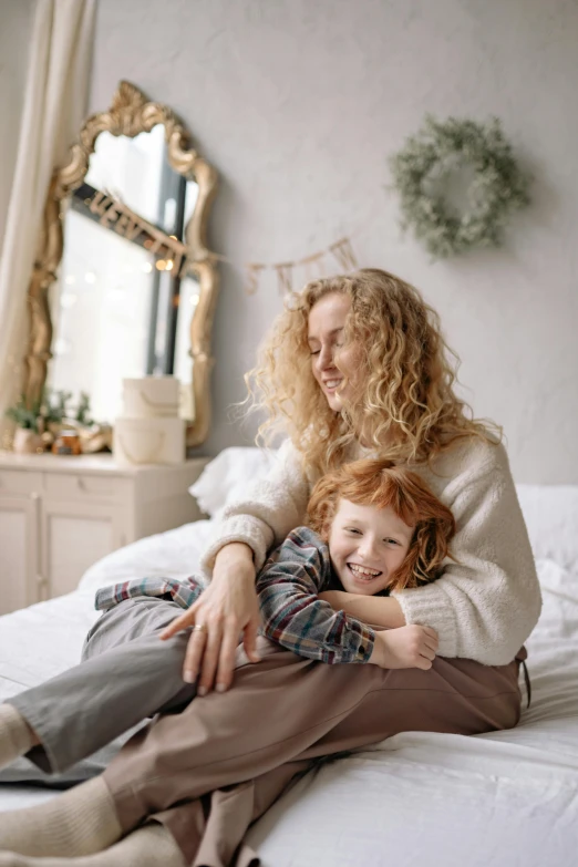 a woman holding a young child while they're sitting on the bed