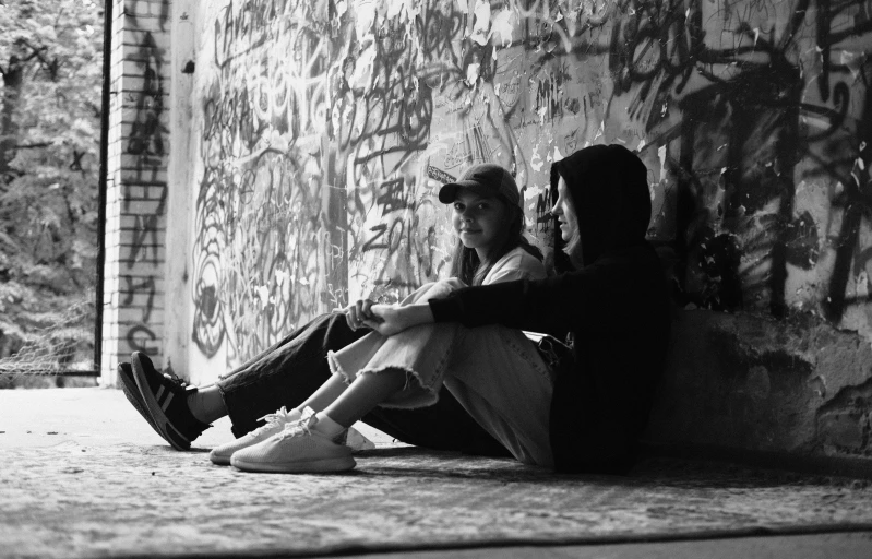 two people sitting against a wall with graffiti