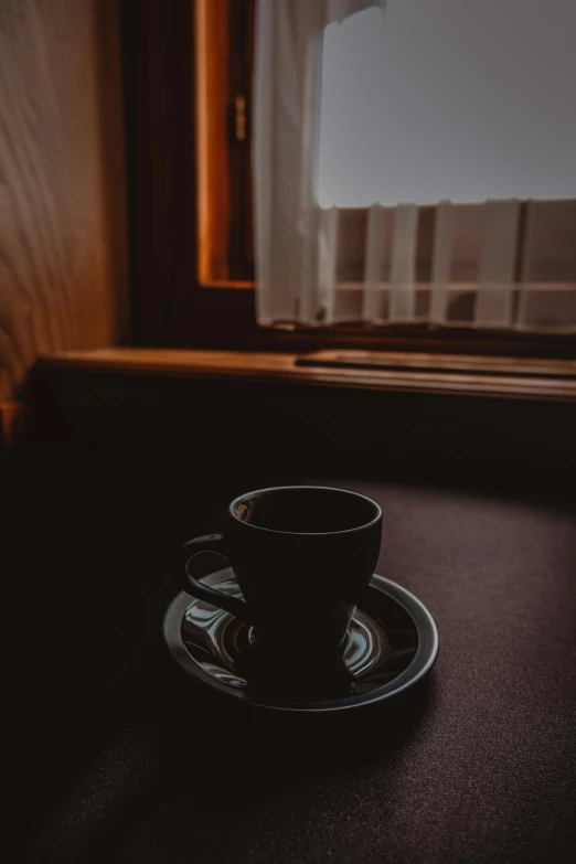 a black saucer sitting on a dark surface near a window
