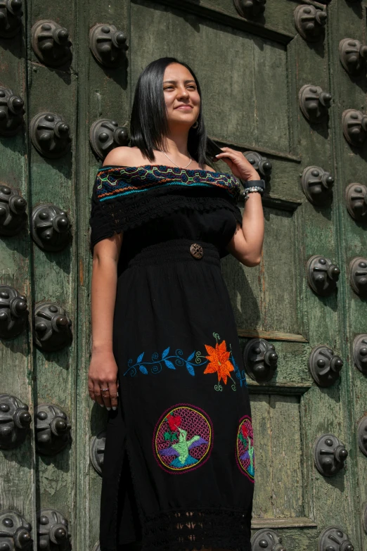 a woman poses in front of a green door wearing a black dress