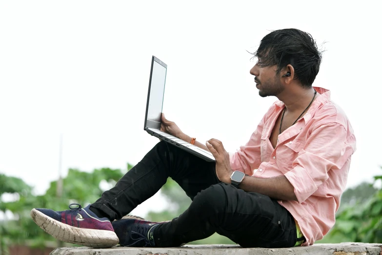 a man sits on a stone ledge and uses his laptop