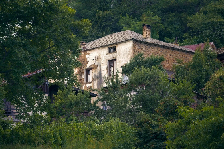 an old house surrounded by trees on the side of a hill