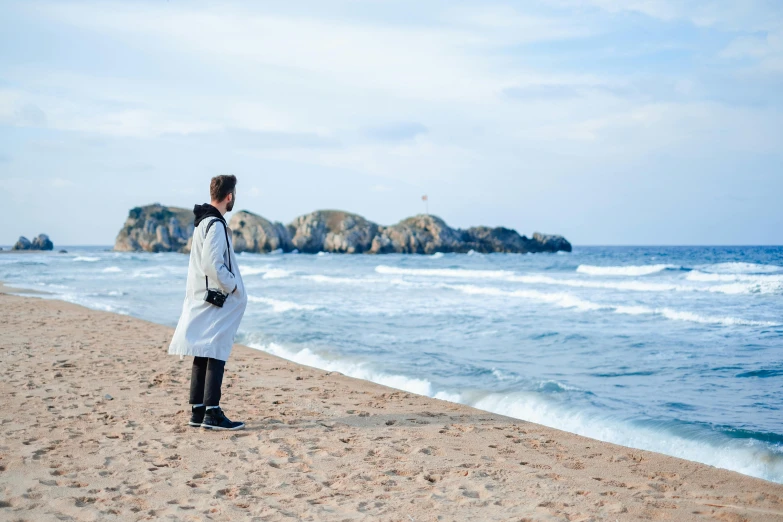 a man in white jacket on beach next to water