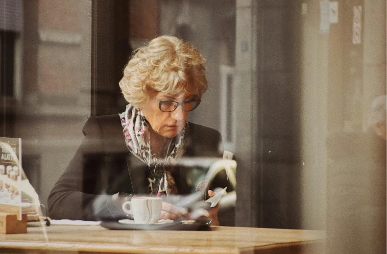 a lady looking at her cell phone and holding a coffee cup