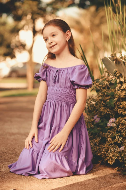 a little girl in a dress is sitting on the ground