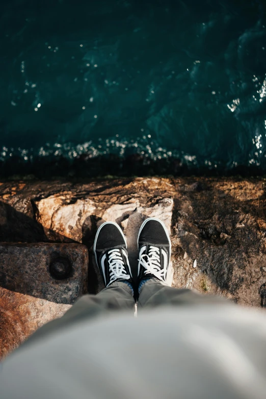 someones feet with white and black sneakers near a body of water
