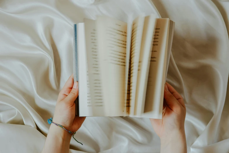 a person laying on top of a bed holding an open book