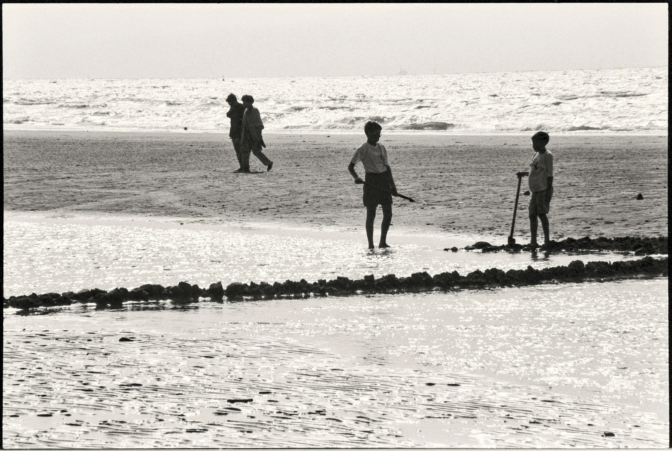 three people standing on the shore watching another person fly a kite