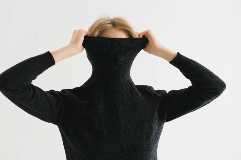 a woman is covering her face with her black turtle neck sweater