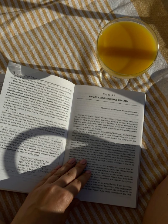 a woman reading a book and looking at a glass of orange juice