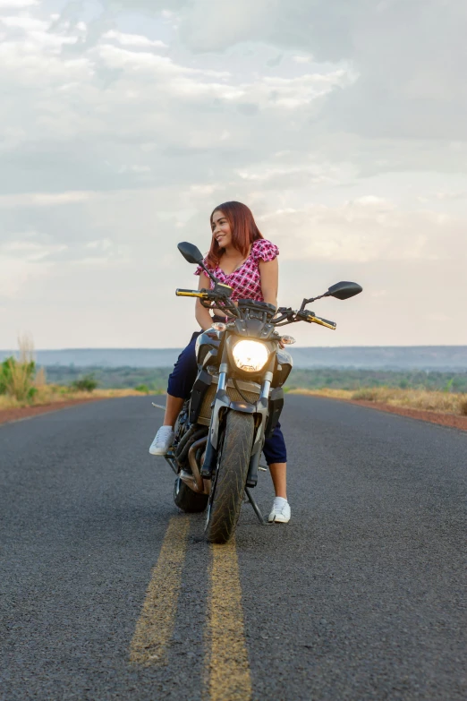 a woman sitting on a motorcycle on a long road