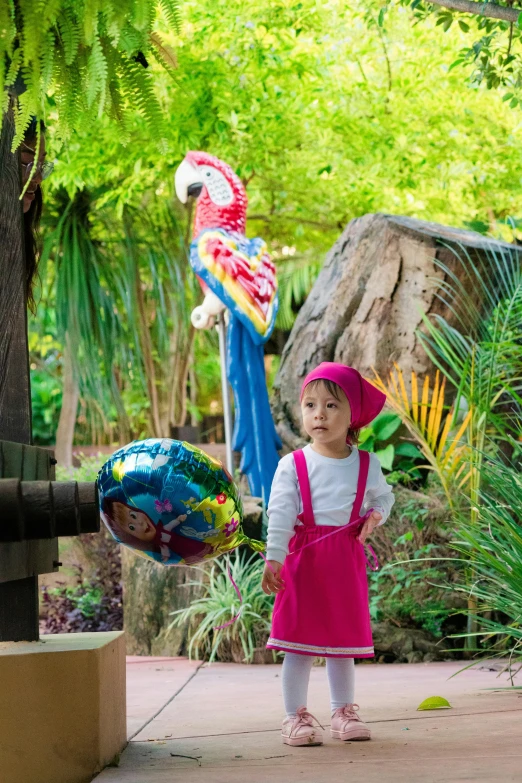 a little girl standing under a tree with a blue parrot sculpture behind her