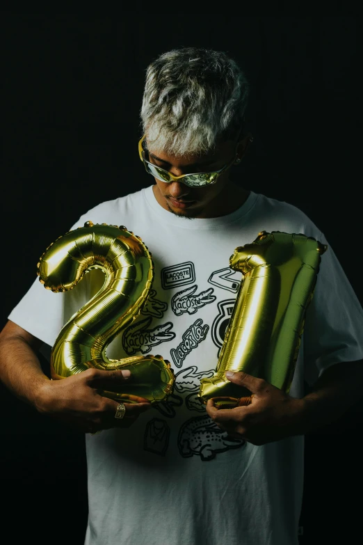 a man is holding some gold balloons and a number 25