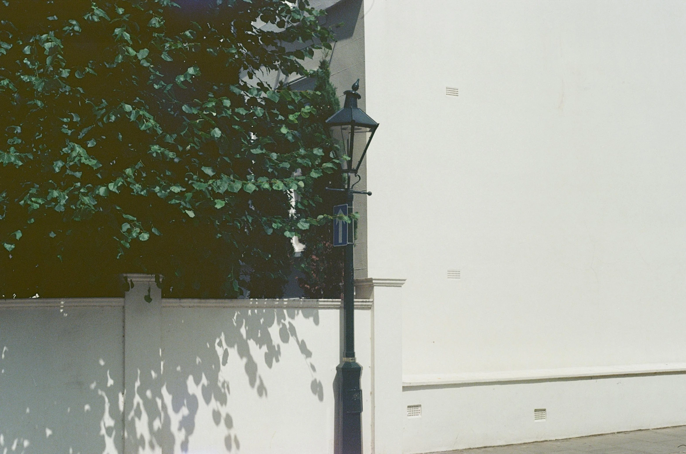 a lamp post in front of a wall, shadow and trees