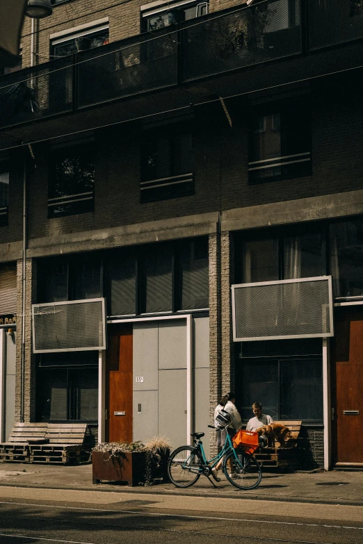 a man walks his bike past a building with two small tables in front of it