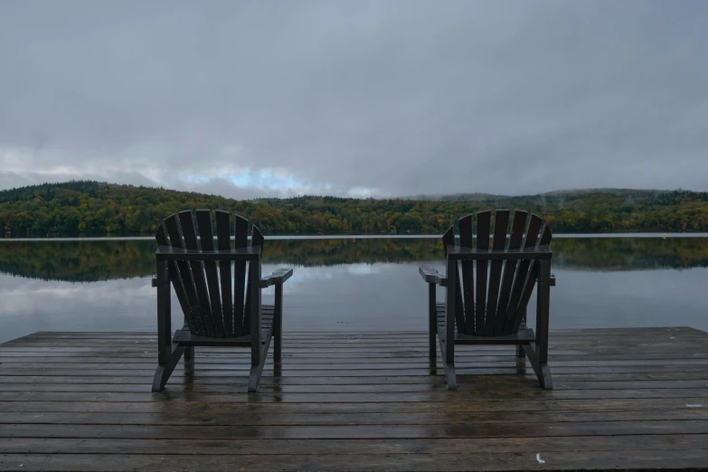 two wooden chairs sitting next to each other on top of a wooden dock