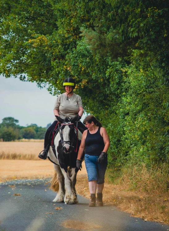 a woman walking behind a white horse next to green trees