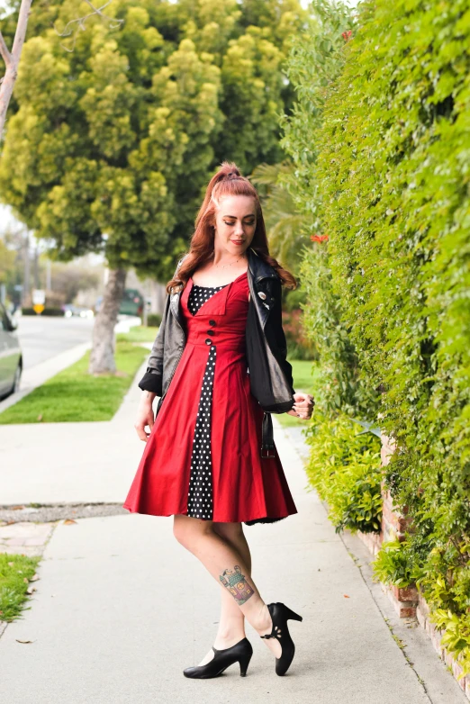 a woman standing on the sidewalk near some bushes