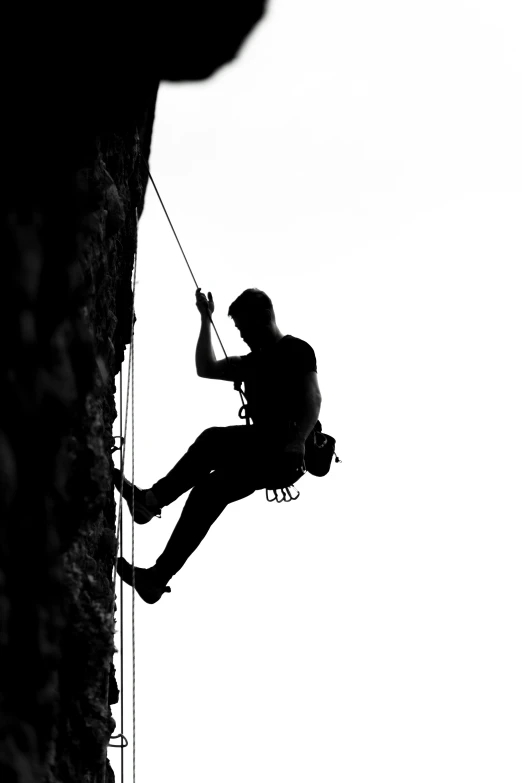 man hanging from the edge of a high cliff while rock climber watches