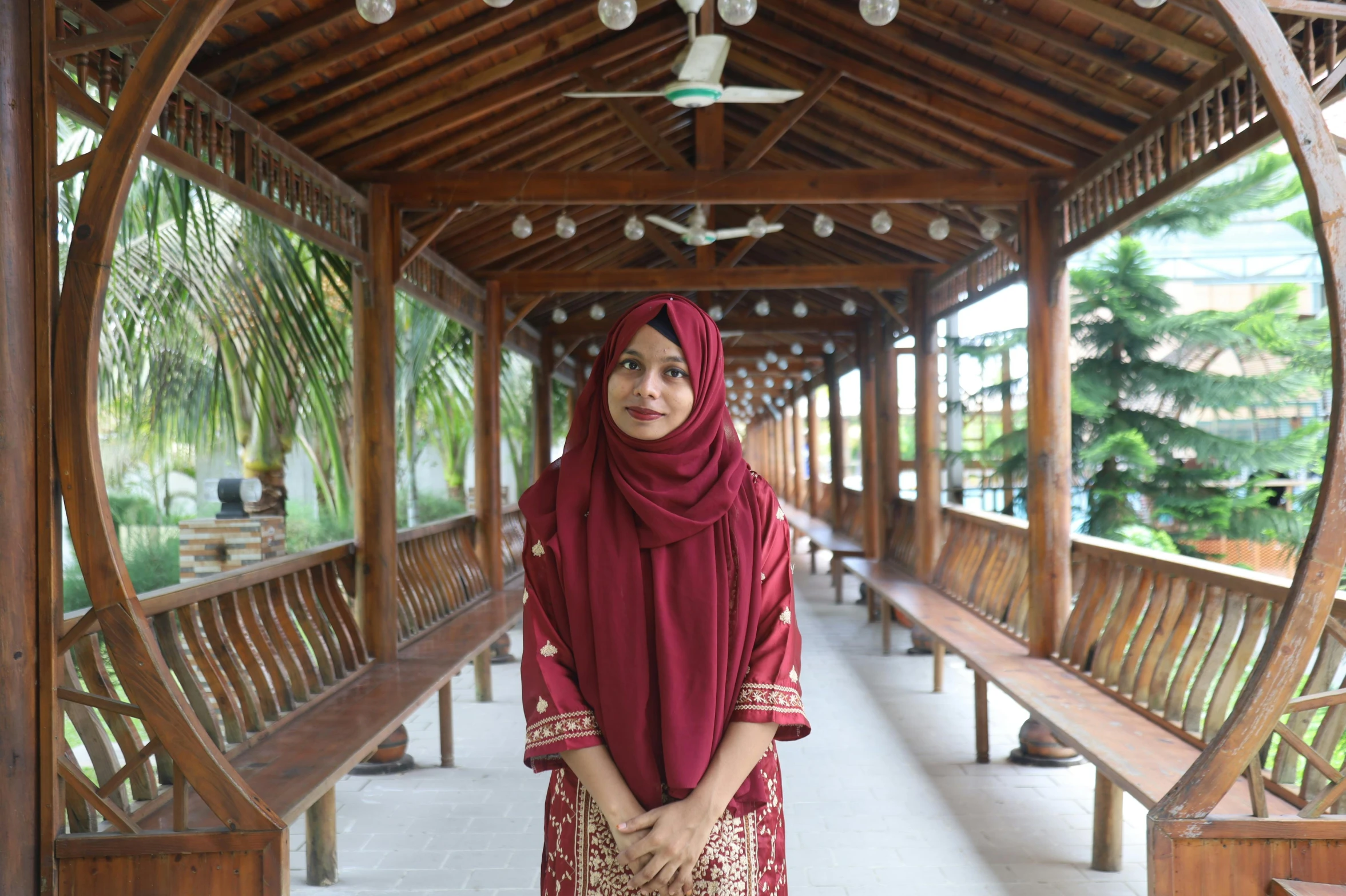 a woman wearing a maroon headscarf and a scarf poses for a po in a building