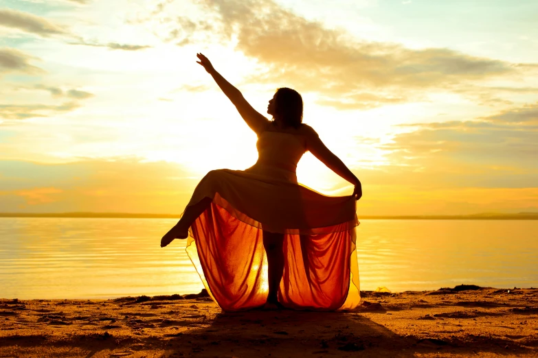 a woman sitting on the beach with her hands up